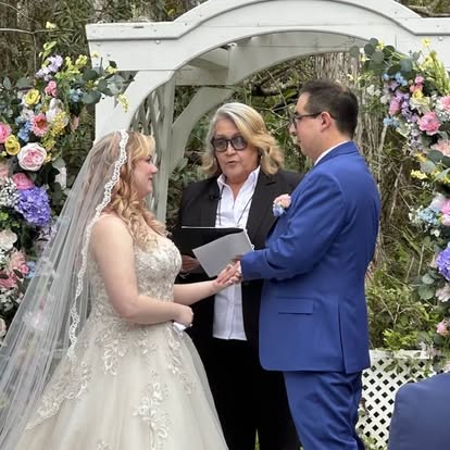 Esther guiding a couple through their vows beneath a flower-covered arbor